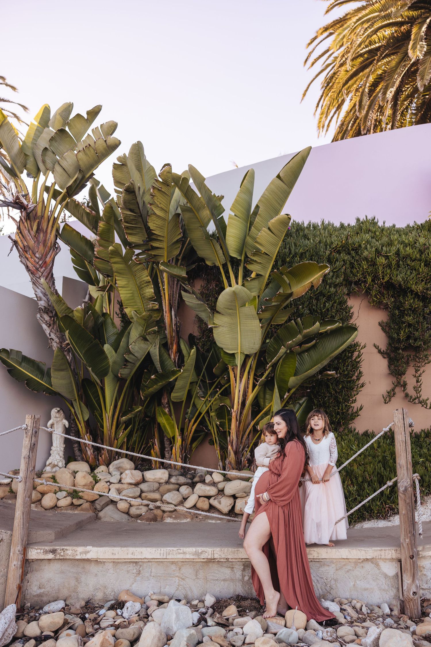 People posing together on stone steps with large tropical banana plants and palm trees in a garden setting at sunset.