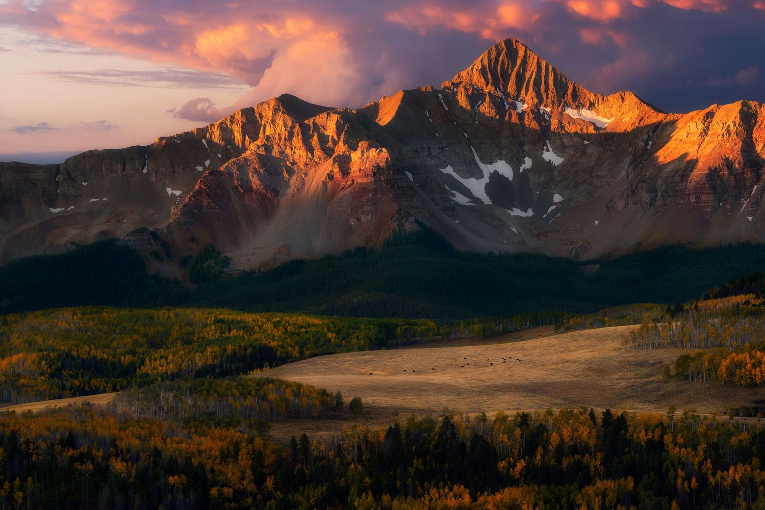 Jagged mountain peaks glowing orange at sunset above autumn valley in Colorado.