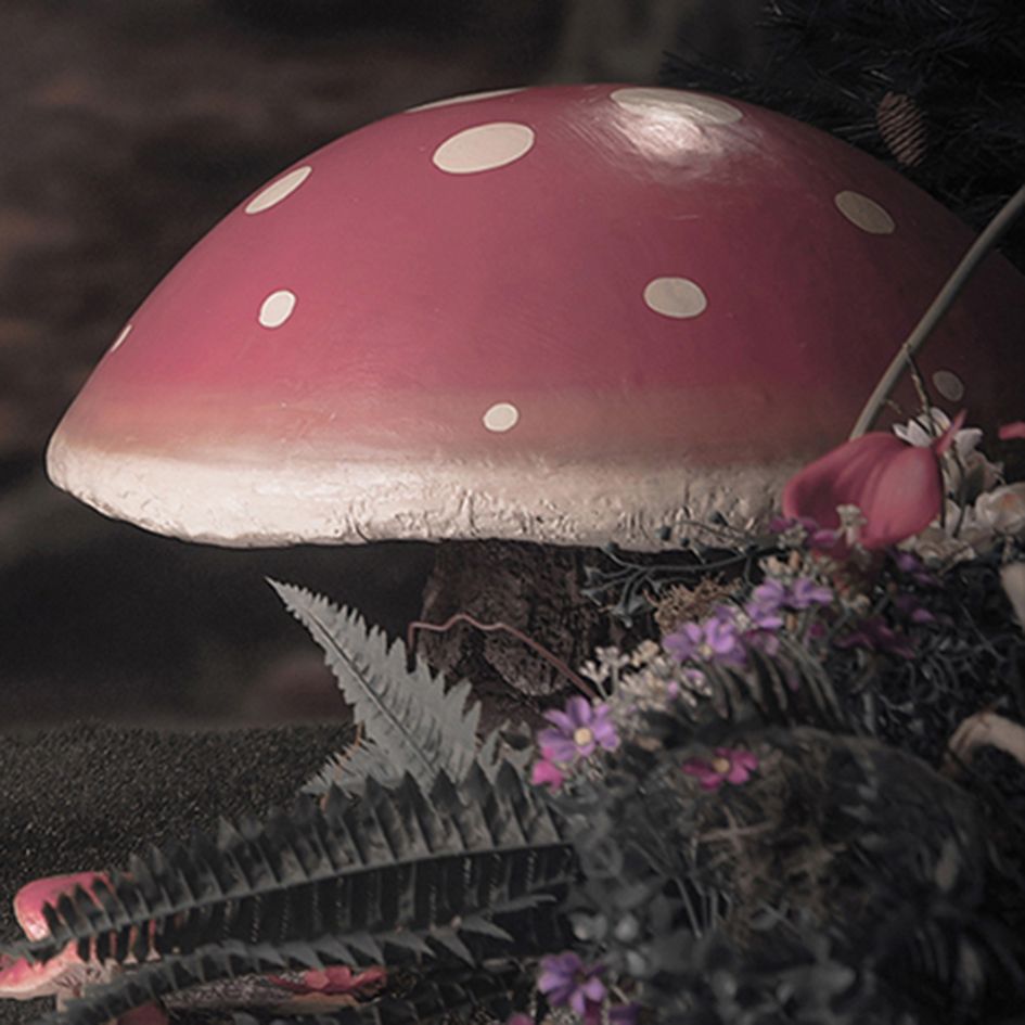 A large red and white spotted mushroom with small purple flowers and ferns in a dark, enchanted forest setting.