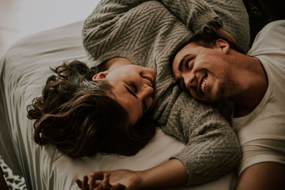 Couple lying on white bedding sharing intimate laughter and joy together.