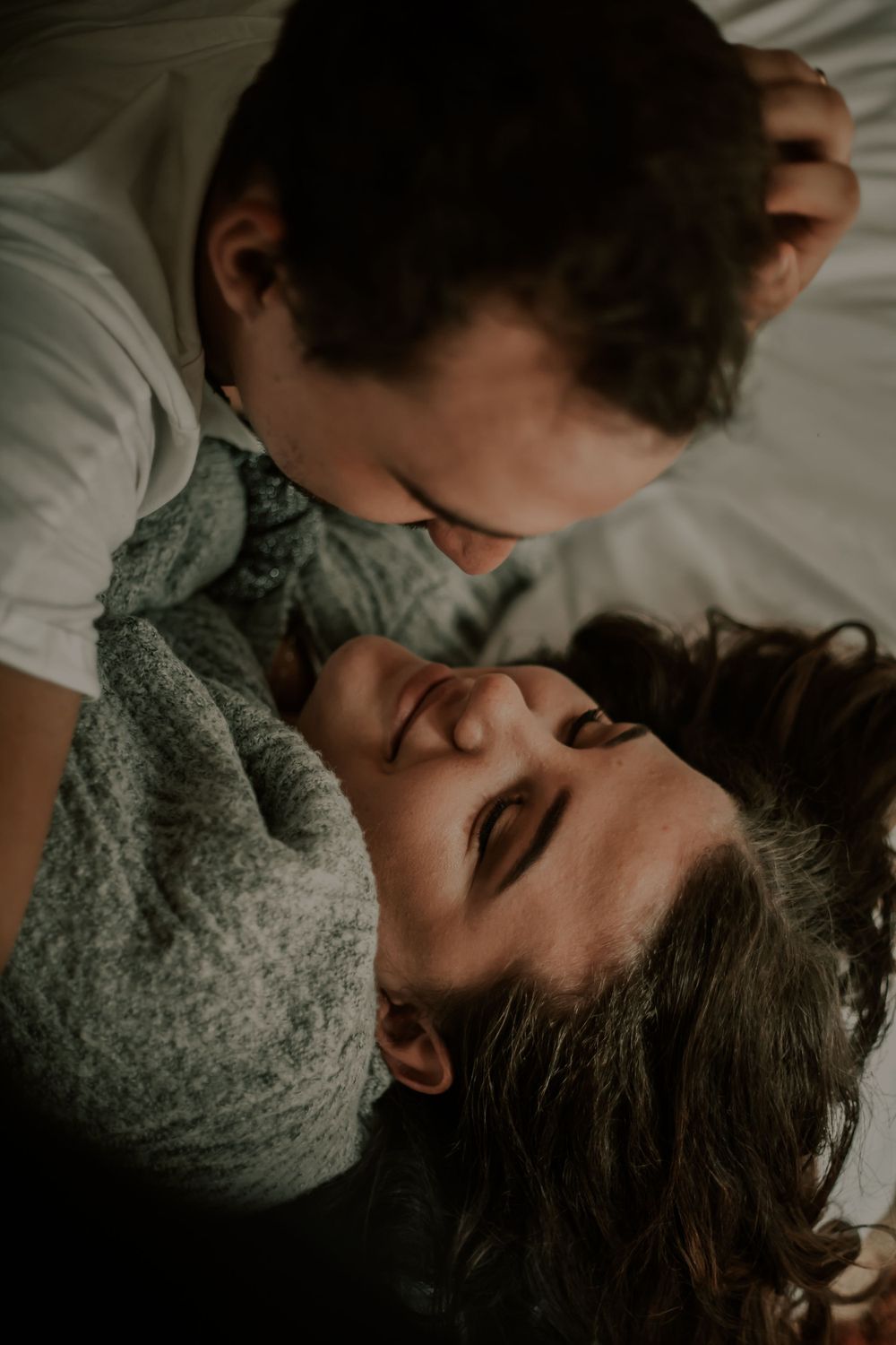 Intimate close-up portrait of couple sharing a tender moment on white bedding.