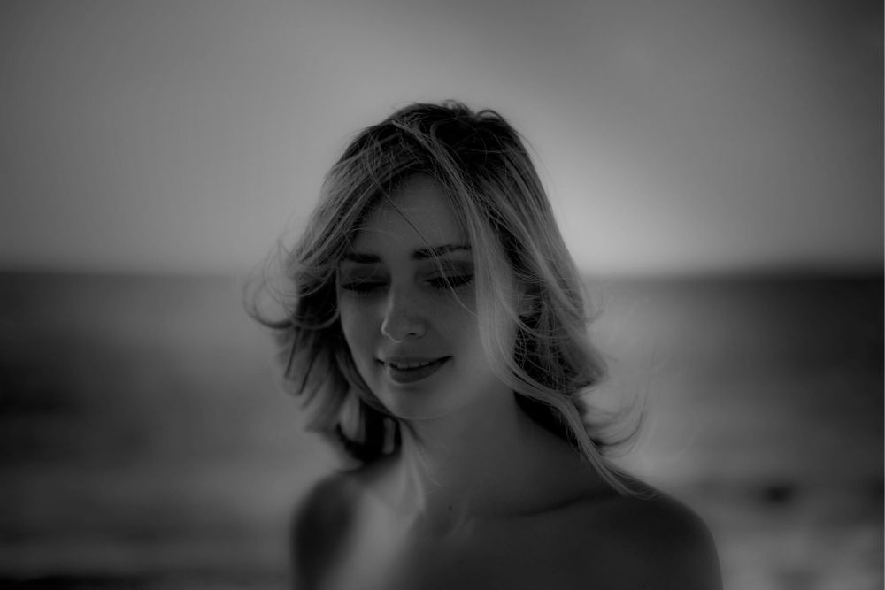 A soft black and white portrait showing a gentle smile and flowing hair against a blurred background.