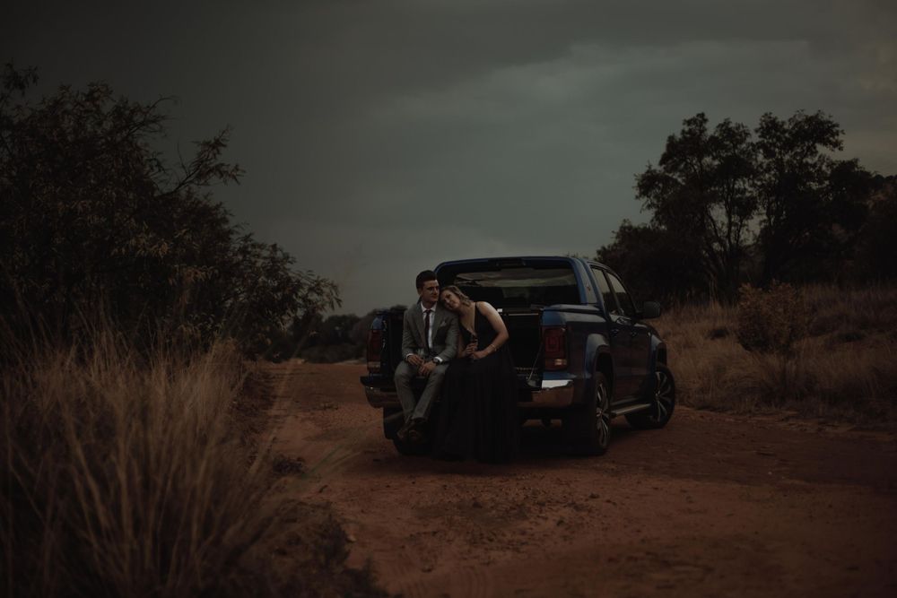 A vintage car parked on a dusty road with dramatic moody lighting and desert brush.