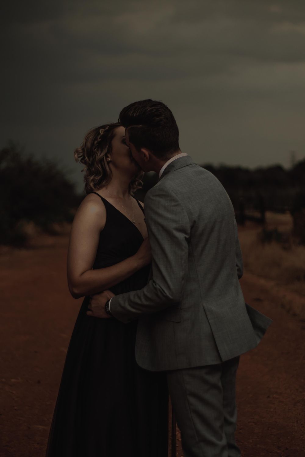 A romantic moment shared between a couple in formal wear on a rustic dirt road at dusk.