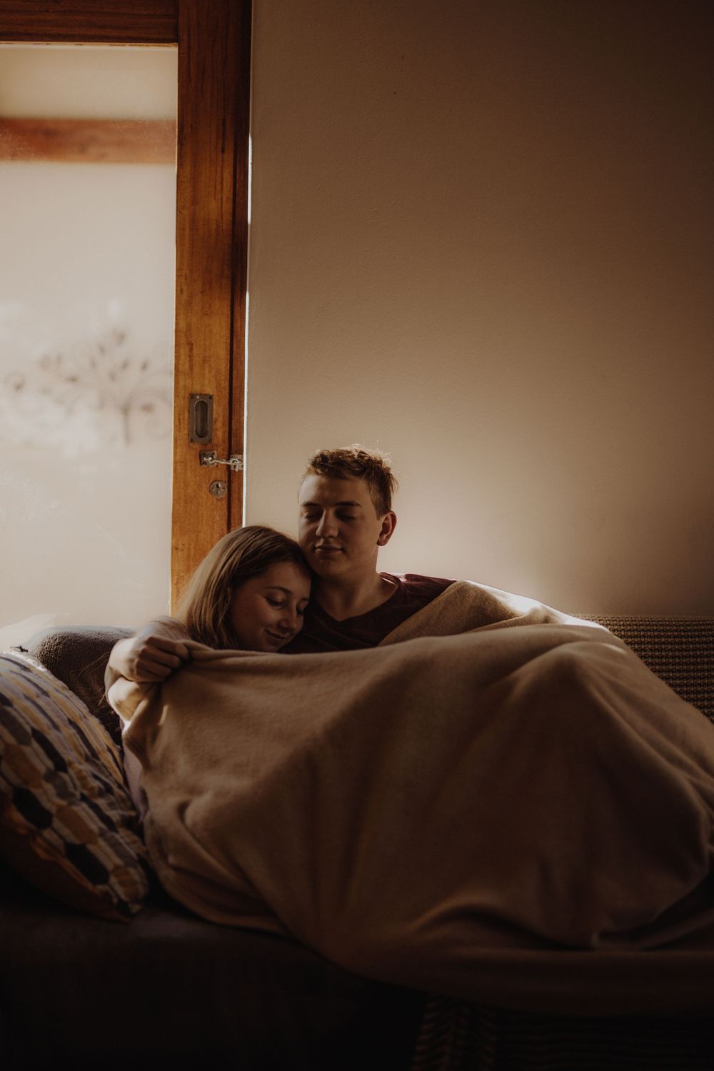 A cozy indoor moment shared under warm blankets in soft natural window light.