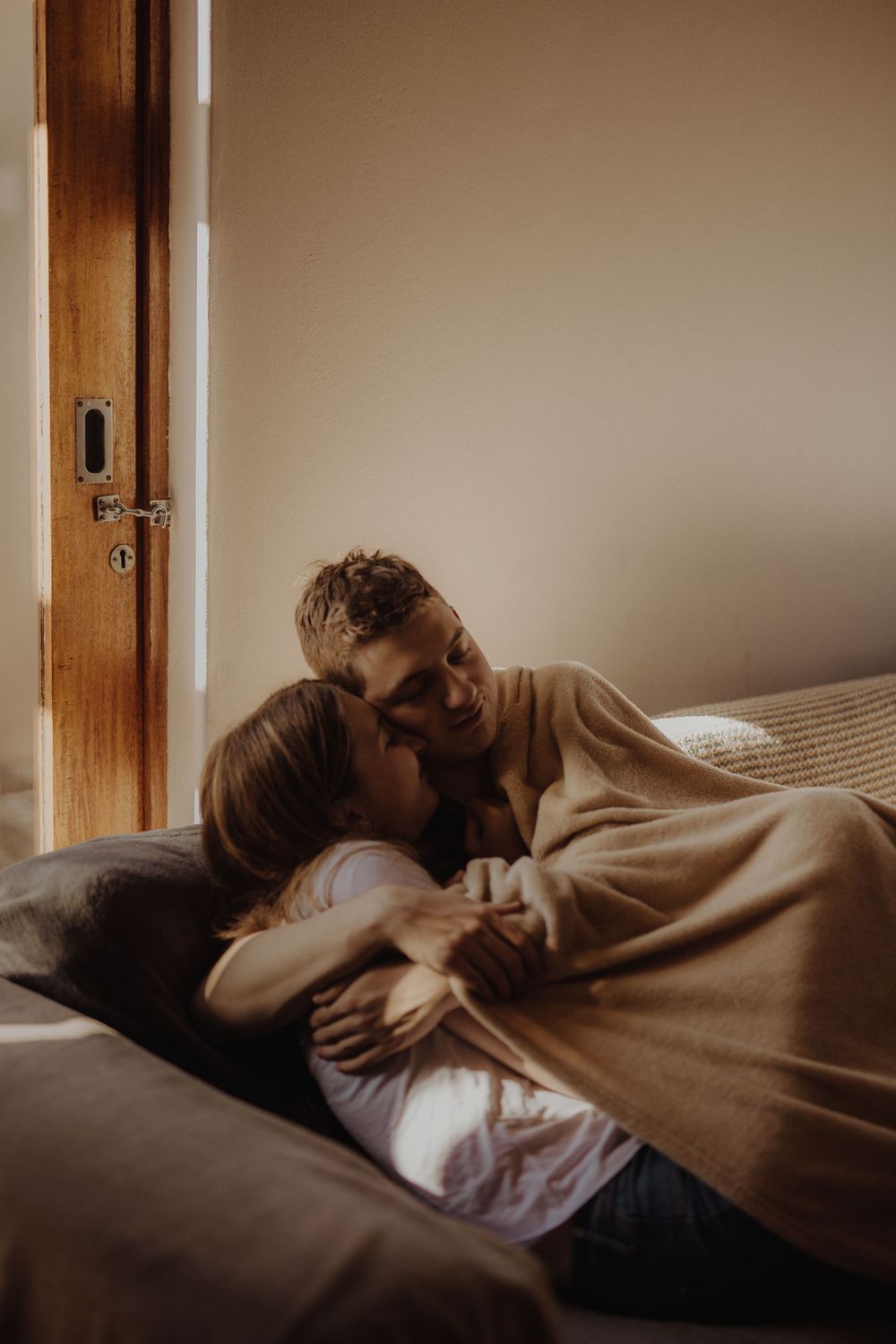 Intimate couple sharing a tender moment while lying together on a bed in warm lighting.