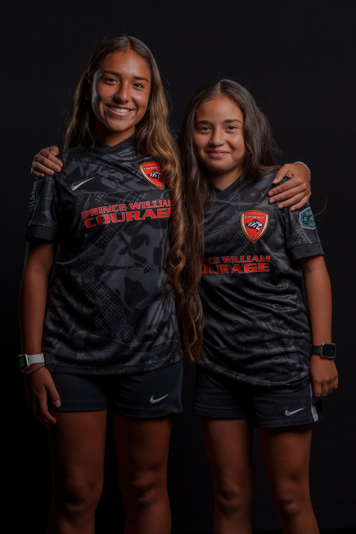 Two athletes wearing red Alexandria jerseys pose together in a playful piggyback portrait against a gray background.