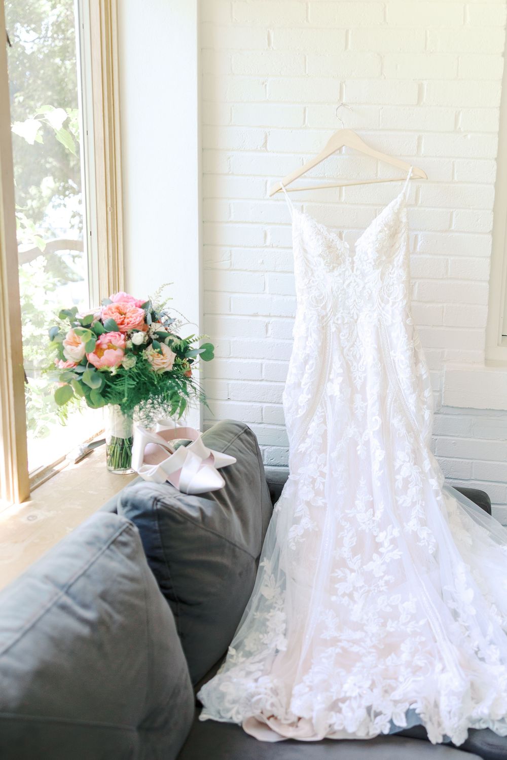 White lace wedding gown displayed against natural light from windows with floral decorations.