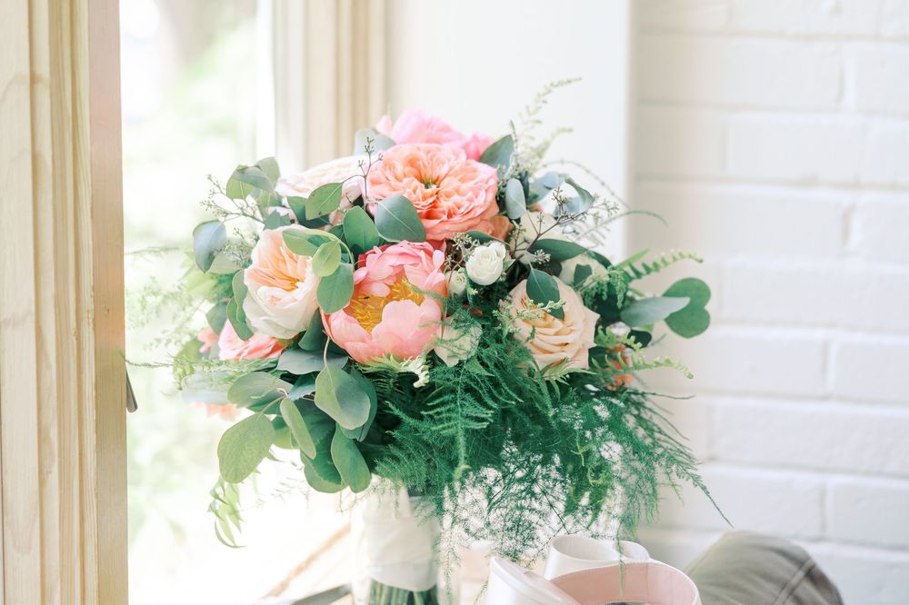 Elegant floral centerpieces with peach roses and eucalyptus displayed against white brick wall with cream curtains.