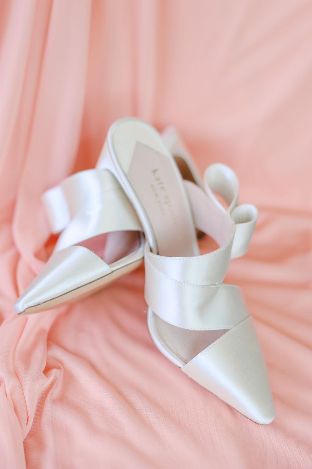 White bridal sandals arranged on pink fabric background.