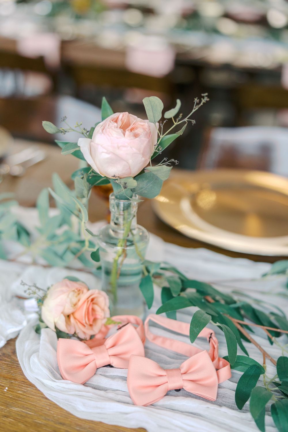 Pink floral centerpiece and bow tie decorations arranged on a classic table setting with gold charger plates.