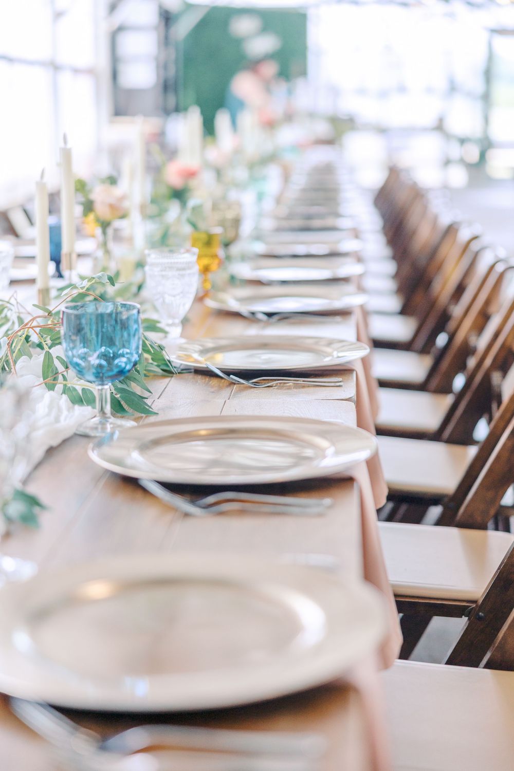 An elegant wedding reception table setting with white linens, place settings and scattered greenery decorations.