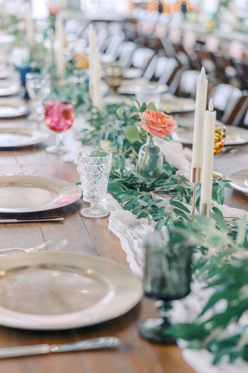 Elegant wedding reception table setting with greenery, candles and crystal glassware.