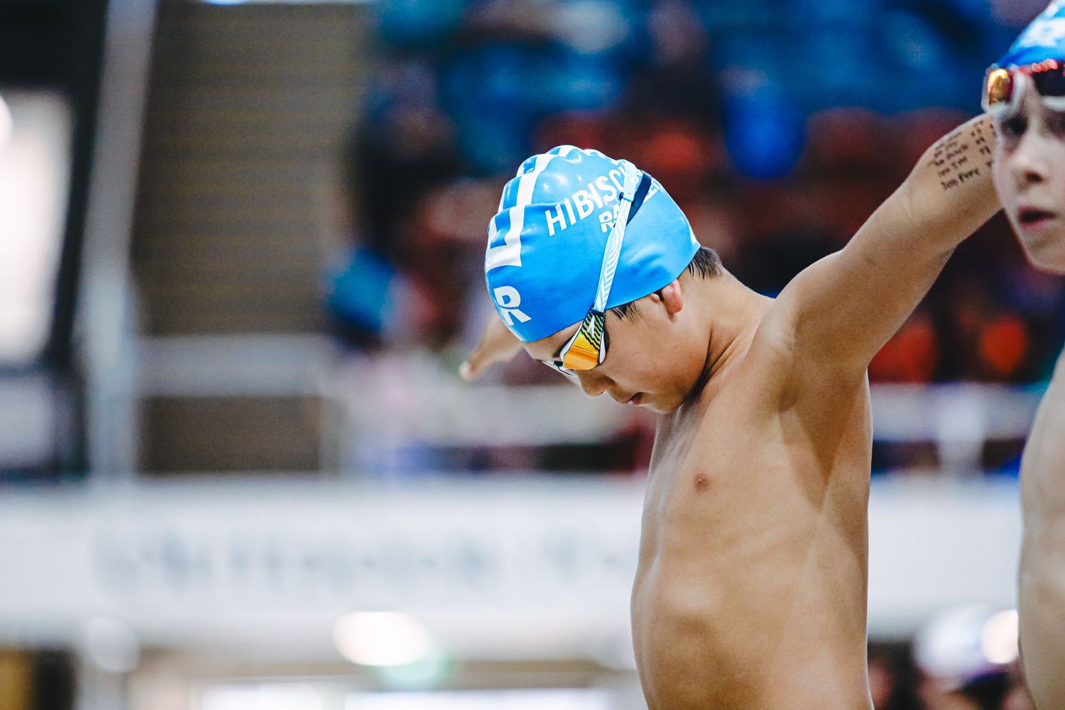 Competitive swimmer wearing bright green cap and goggles performs breaststroke in indoor pool during race.