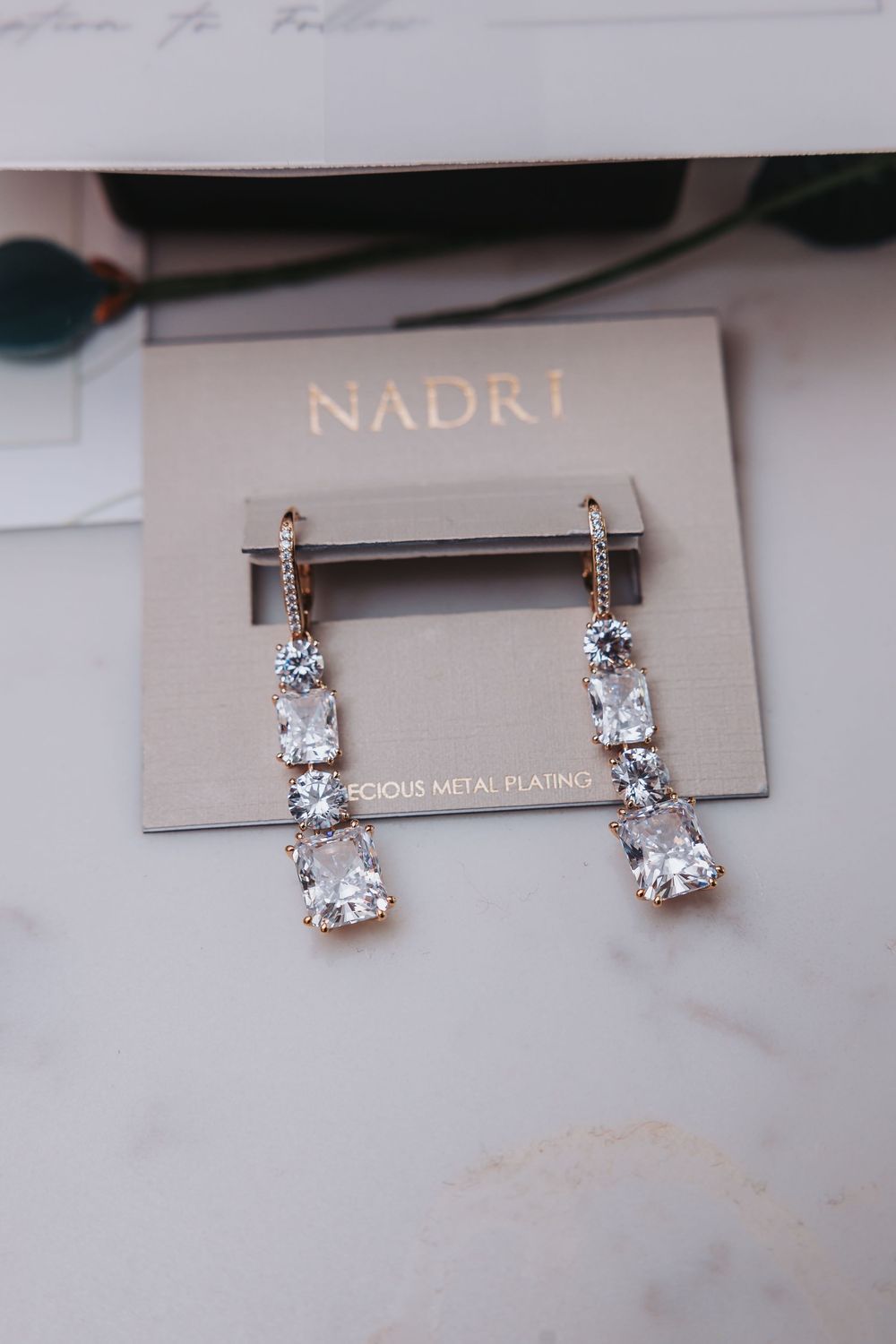 Elegant Nadri crystal drop earrings displayed on a light gray background with rose gold plating details.
