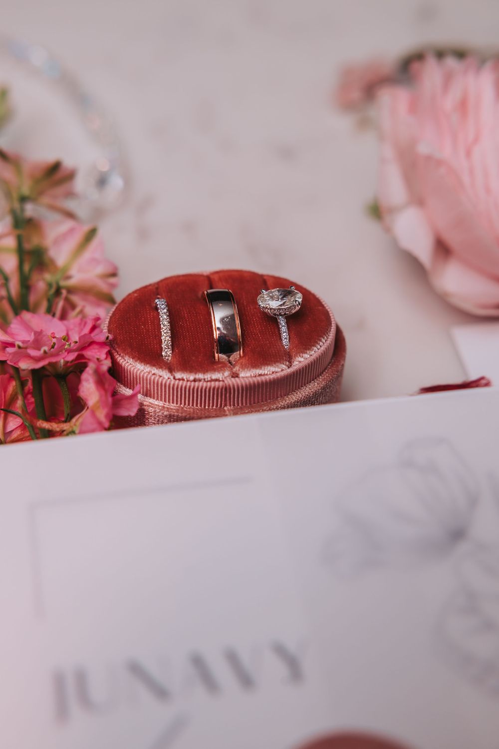 Wedding rings displayed on a pink velvet ring box surrounded by delicate flowers and wedding decor.