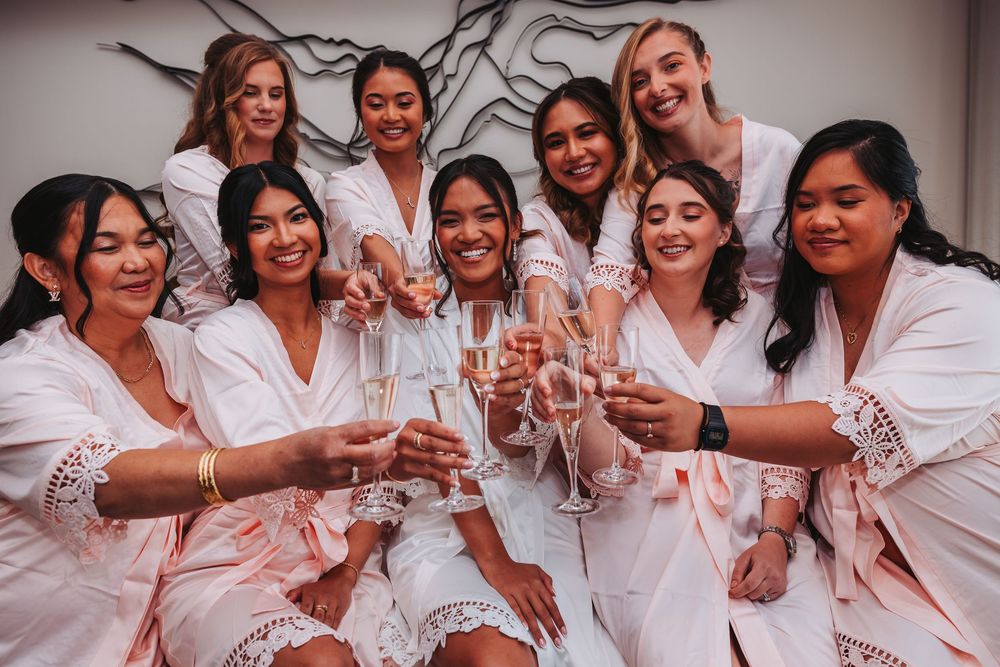 A group in matching white robes celebrates joyfully together during a pre-wedding gathering.