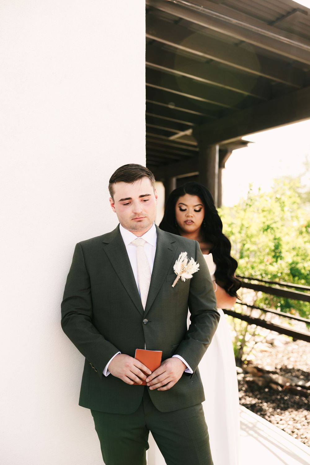 Wedding couple in formal attire standing against a modern white building exterior.