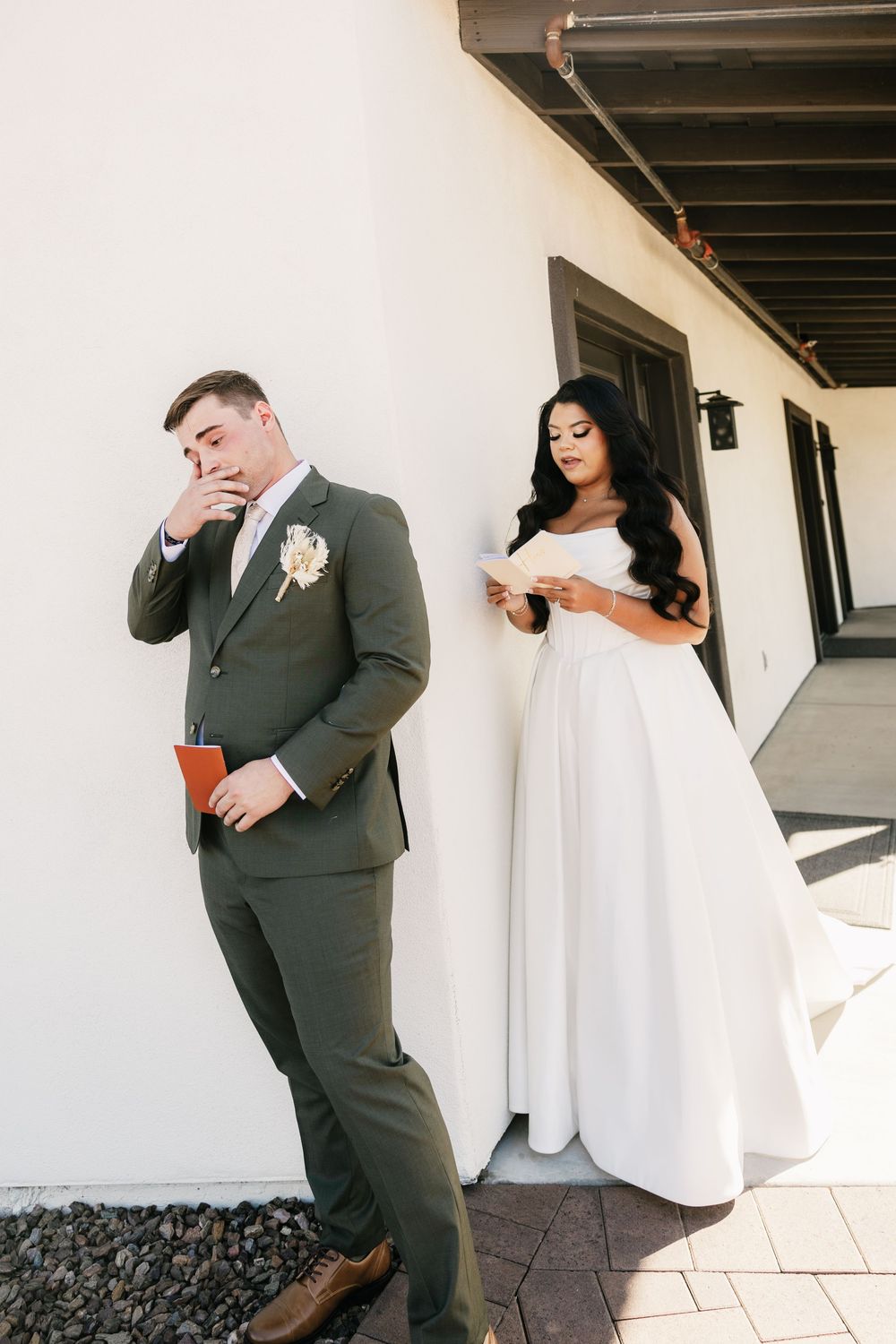 Playful first look wedding photos captured against a white building exterior.