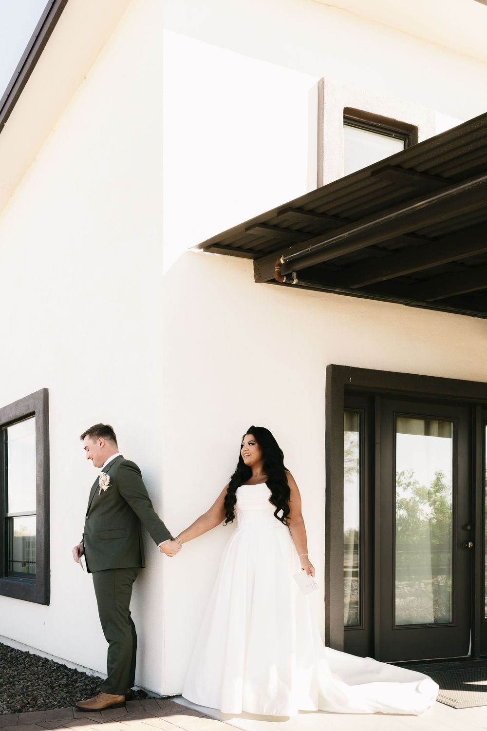 Wedding couple plays hide and seek around modern white building exterior with black windows.