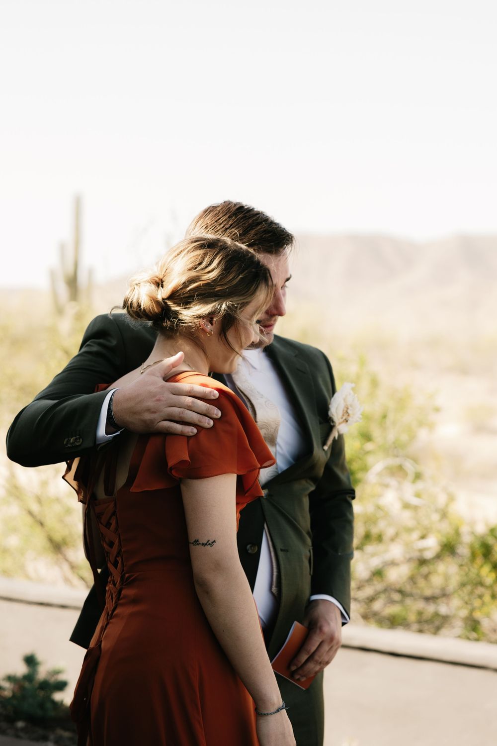 Emotional first look moment captured in warm sunlight against desert backdrop.