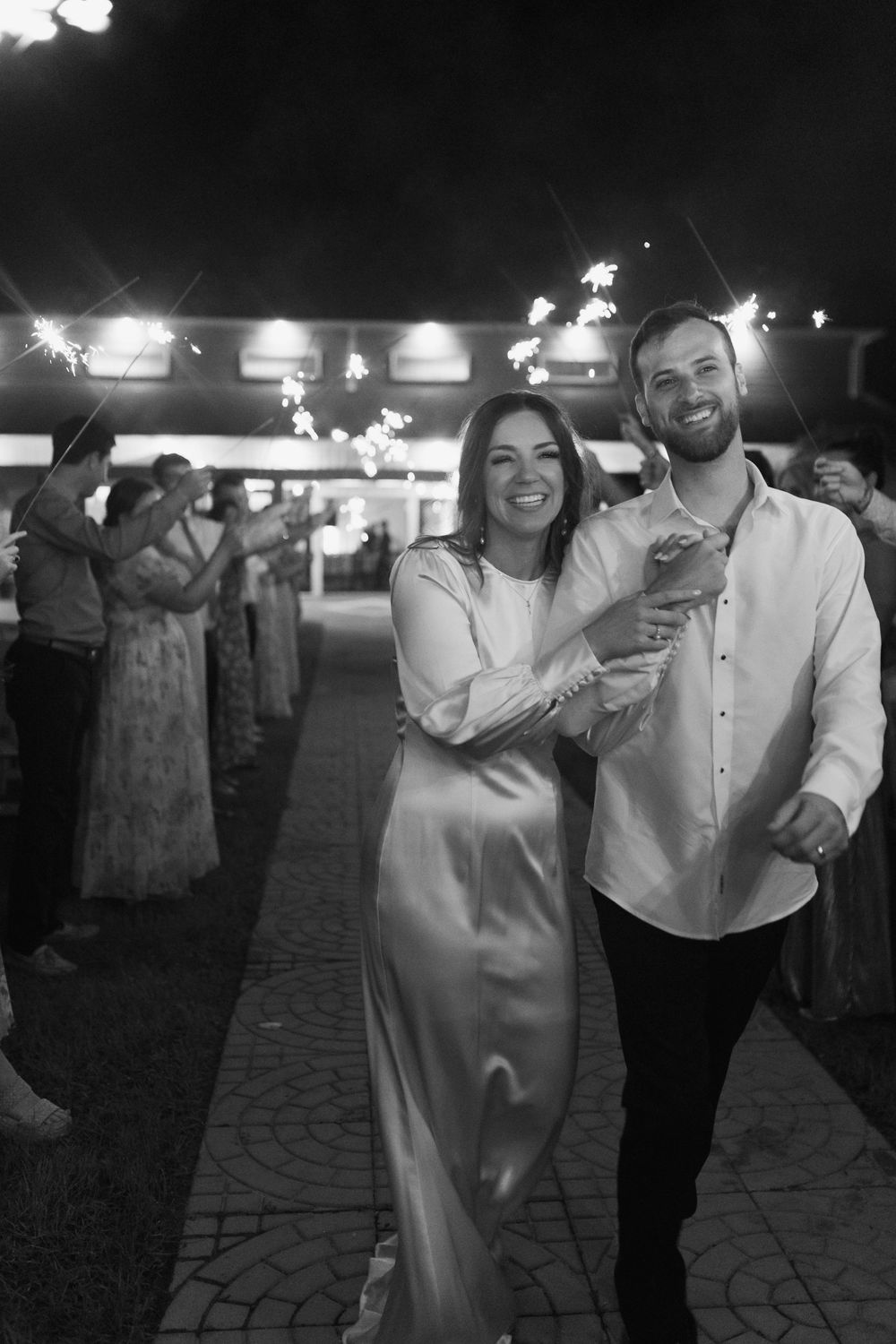 Wedding guests dance and celebrate at a nighttime outdoor reception under lights.