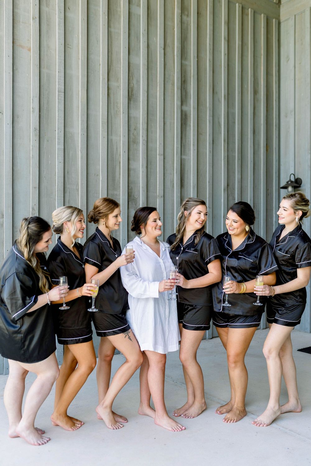 Bridesmaids in matching navy robes create a playful lineup pose against a wooden wall.