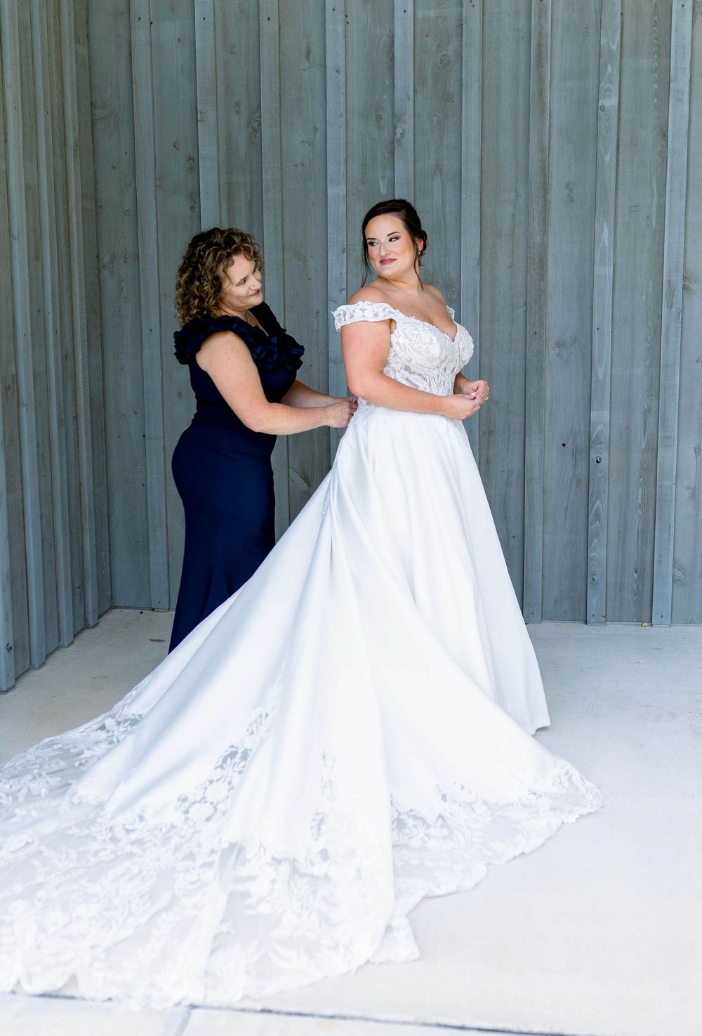 A wedding dress with intricate lace details and long train being adjusted in a modern setting.