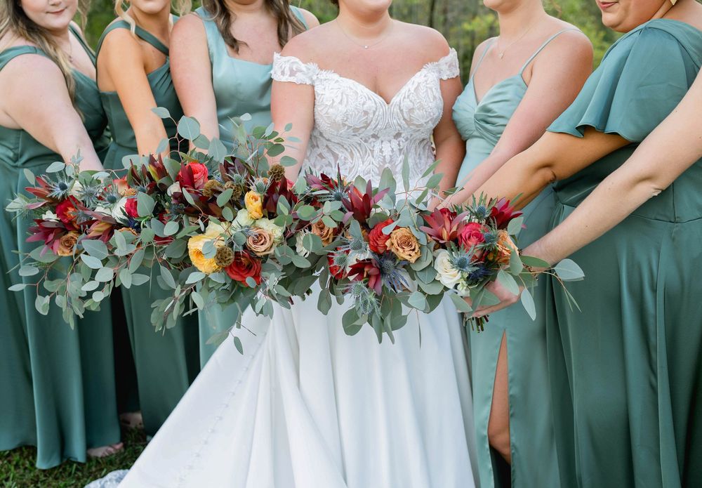 Bridesmaids in sage green dresses hold colorful bouquets in an elegant wedding party lineup.