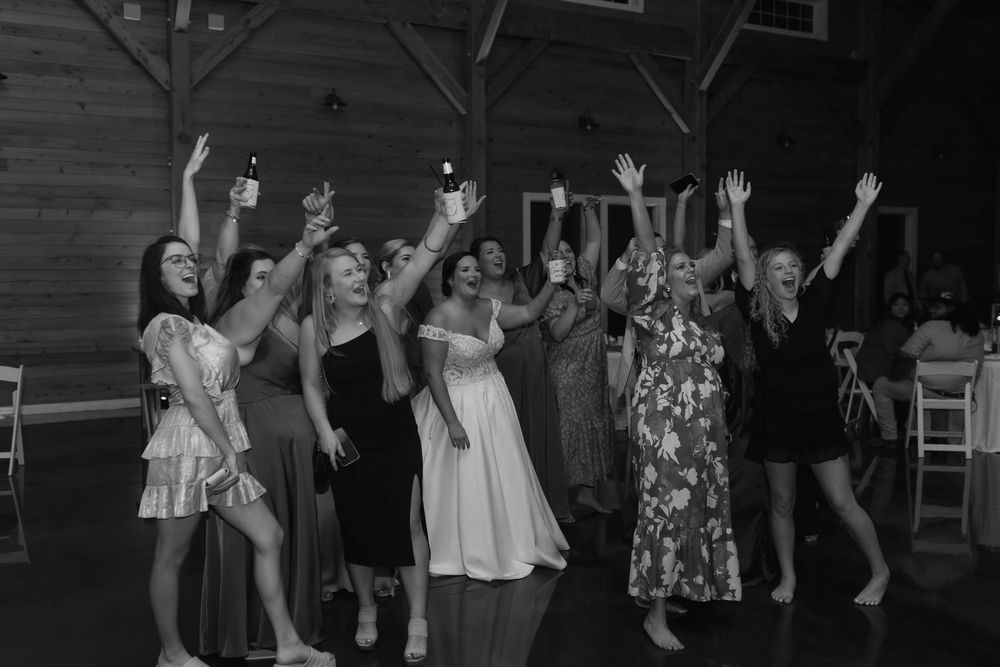 Wedding reception guests dancing and celebrating with raised arms in a dark venue.