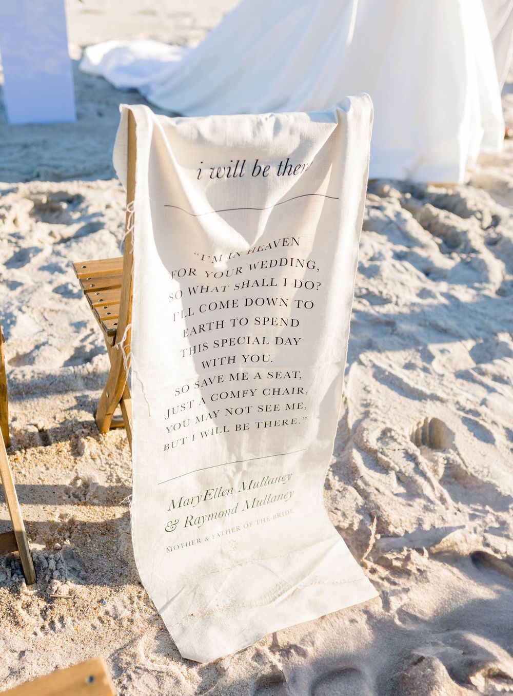 Wedding programs and signage lay scattered on white sand at a beach wedding ceremony.