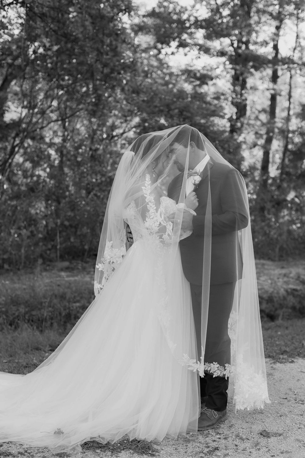 A flowing white wedding dress and veil creates an ethereal silhouette against trees in a garden setting.
