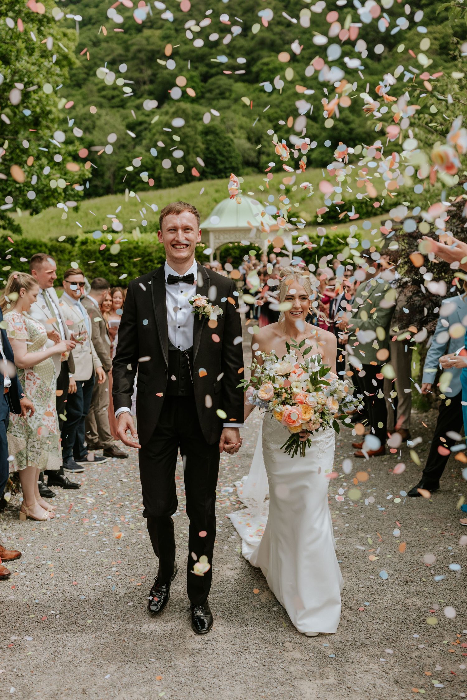 Wedding couple poses together on green lawn with rustic lodge and wooded hillside in background.