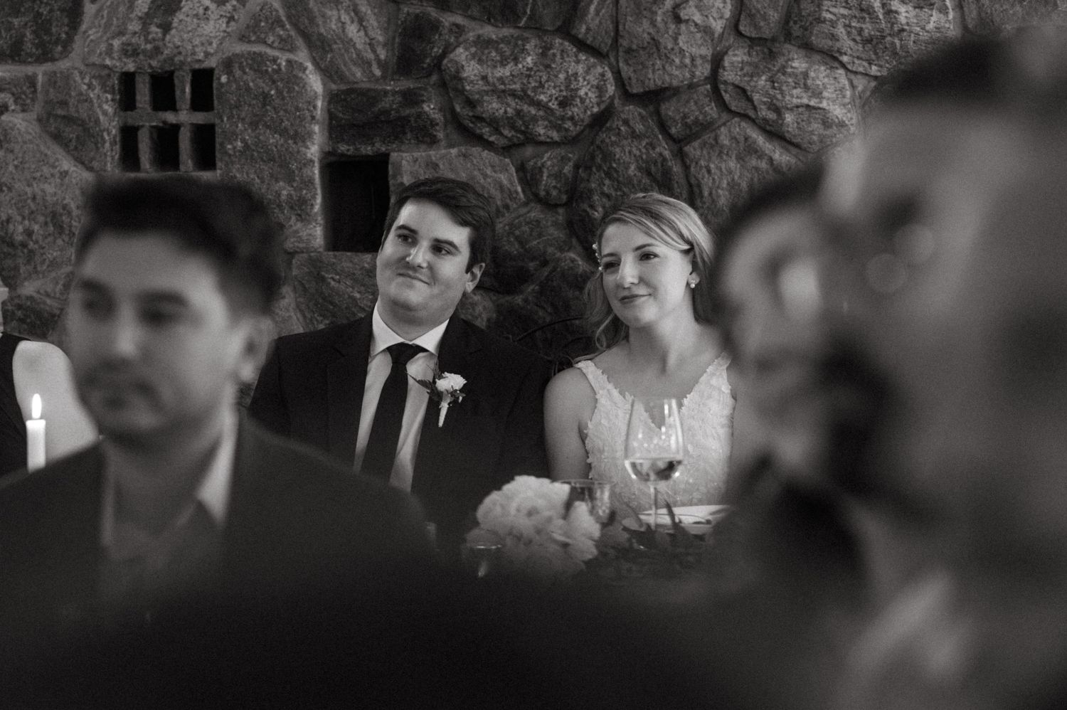 Black and white candid moment showing a happy couple sitting together during a wedding reception at Northridge Inn, Muskoka