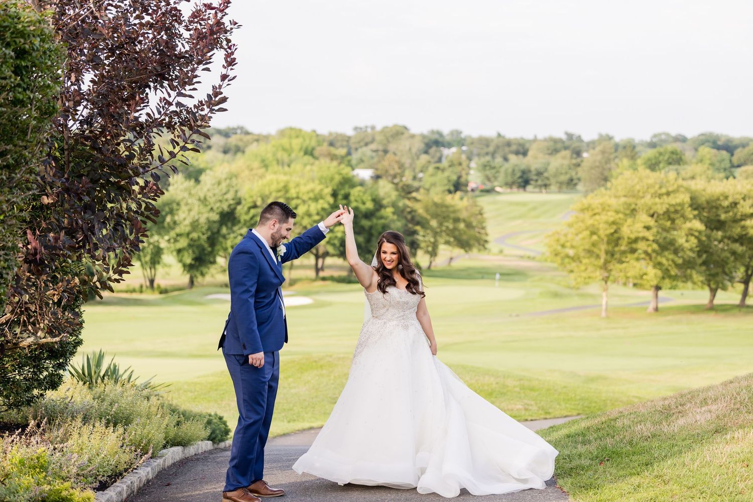 A couple in wedding attire celebrates joyfully in a scenic golf course setting with lush green grass and trees.