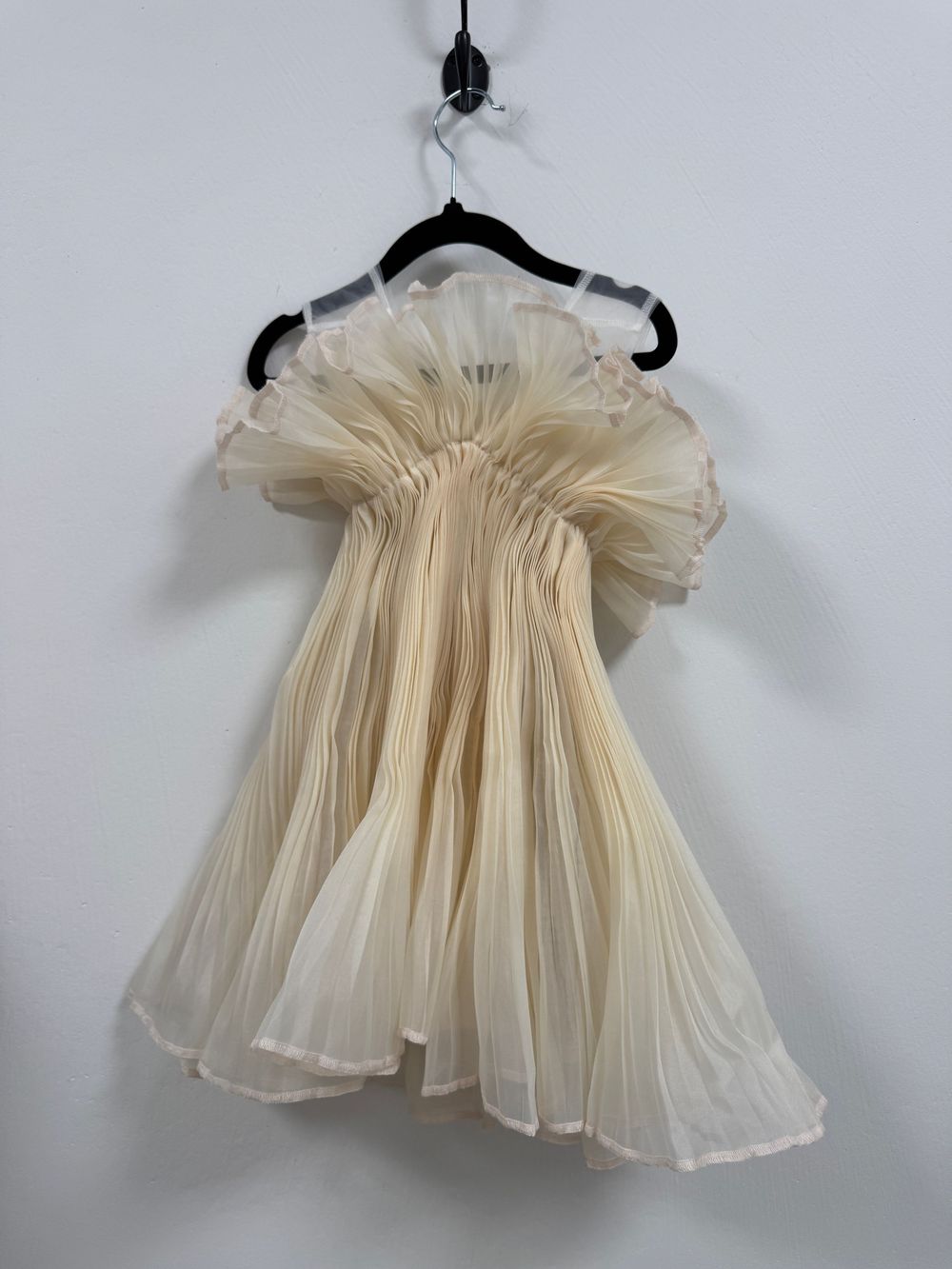 Vintage cream-colored pleated baby dress with sheer fabric shown hanging on dark hangers from different angles.
