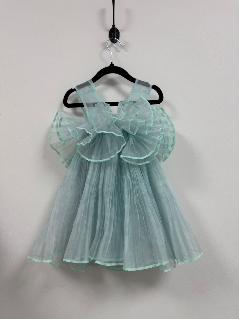 Pale mint green tulle baby dress with bow detail shown from multiple angles on black hangers against white backdrop.