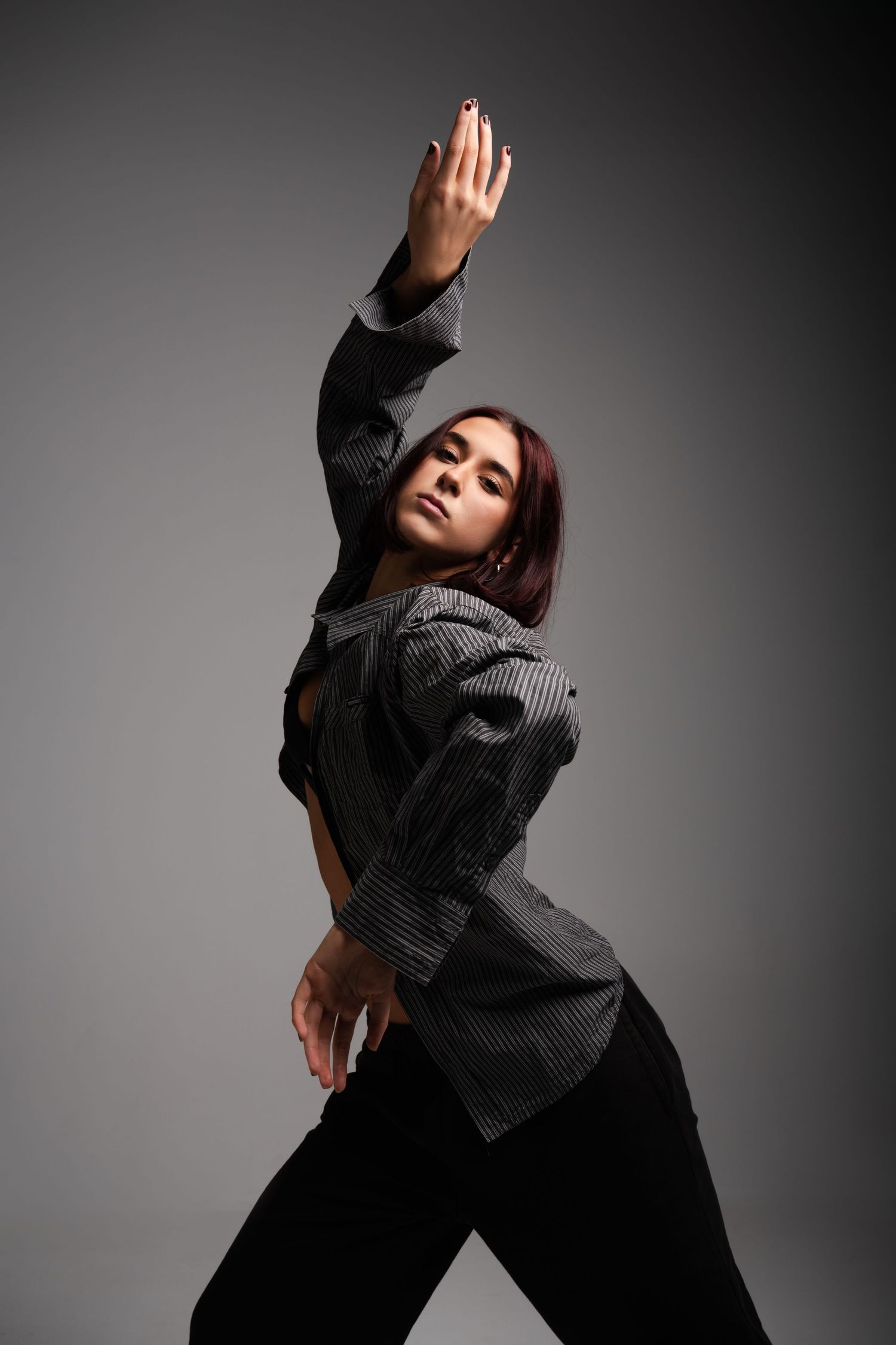 Dancer in a gray sweater and dark pants performs expressive movements against a gray studio backdrop.