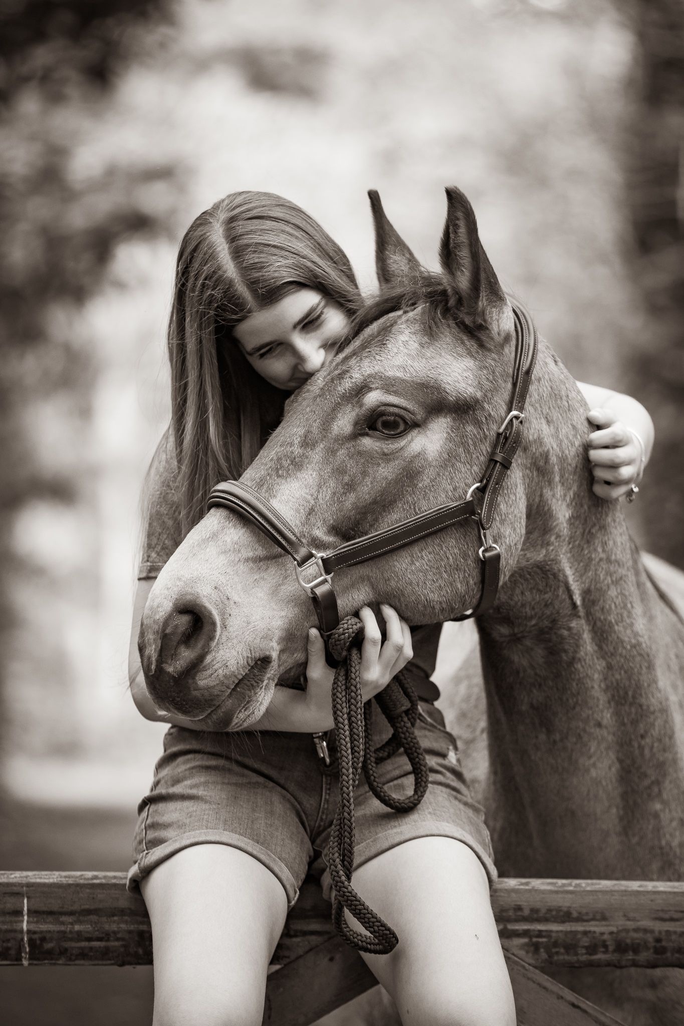 A gentle moment between a rider and dark horse with white blaze in a rustic stable setting, captured in black and white.