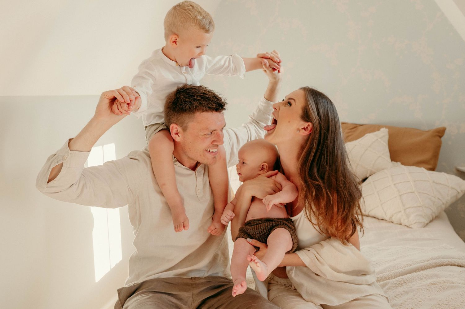 Family having playful moment together on white bed in bright room.