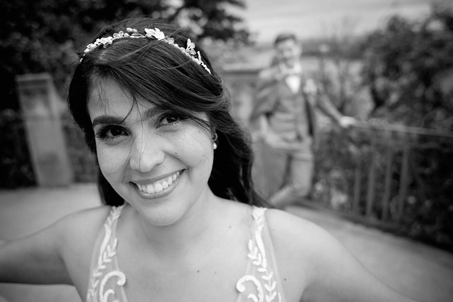 Photograph showing a bride with dark hair in a white wedding dress posing at an outdoor venue.