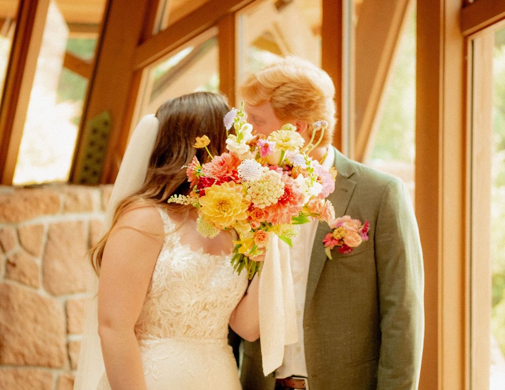 A couple holds a vibrant bouquet of yellow and pink flowers during their wedding ceremony.