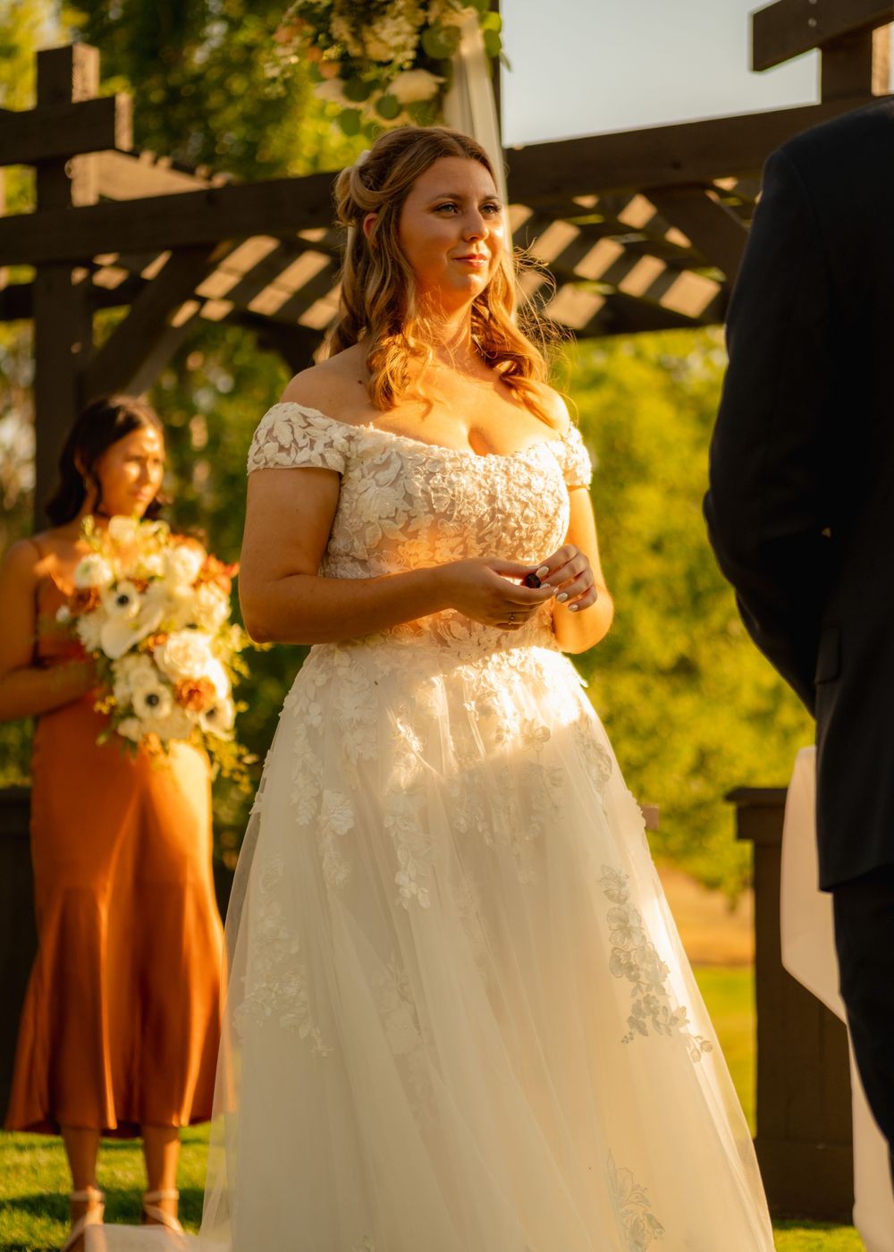 Bride in lace wedding dress during outdoor ceremony with sunset golden light.