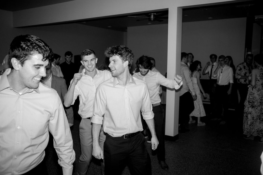 Black and white photo of guests dancing at a lively wedding reception.