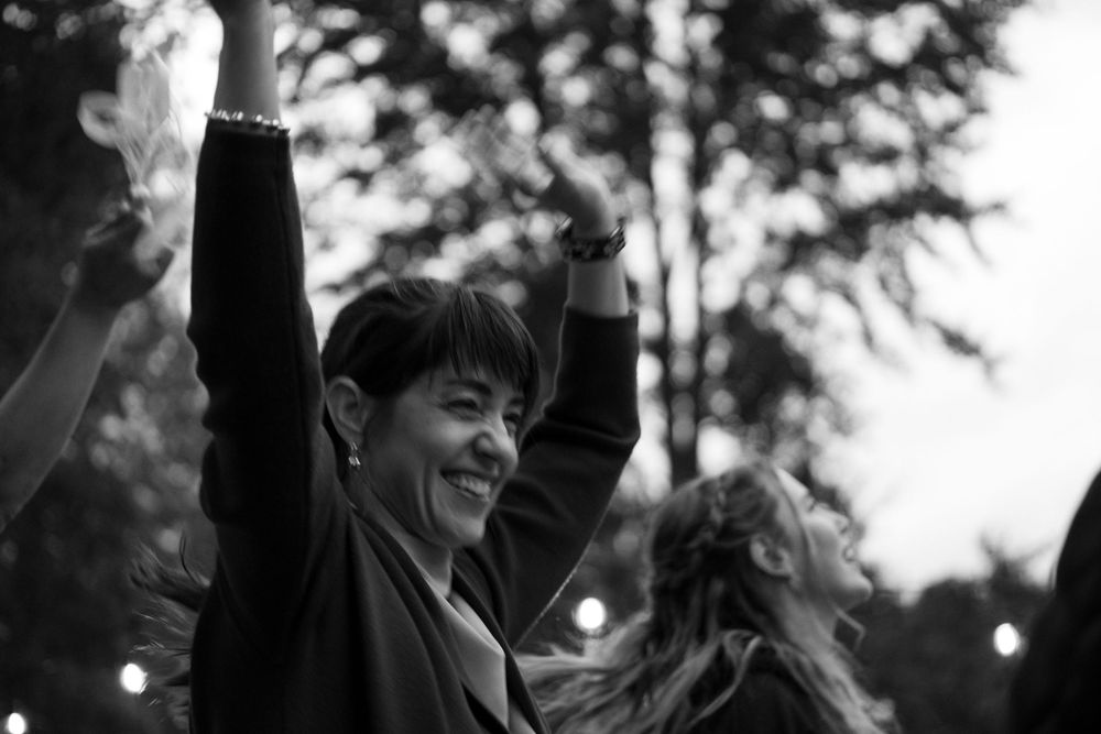 Black and white photo of joyful celebration with raised hands silhouetted against evening sky.