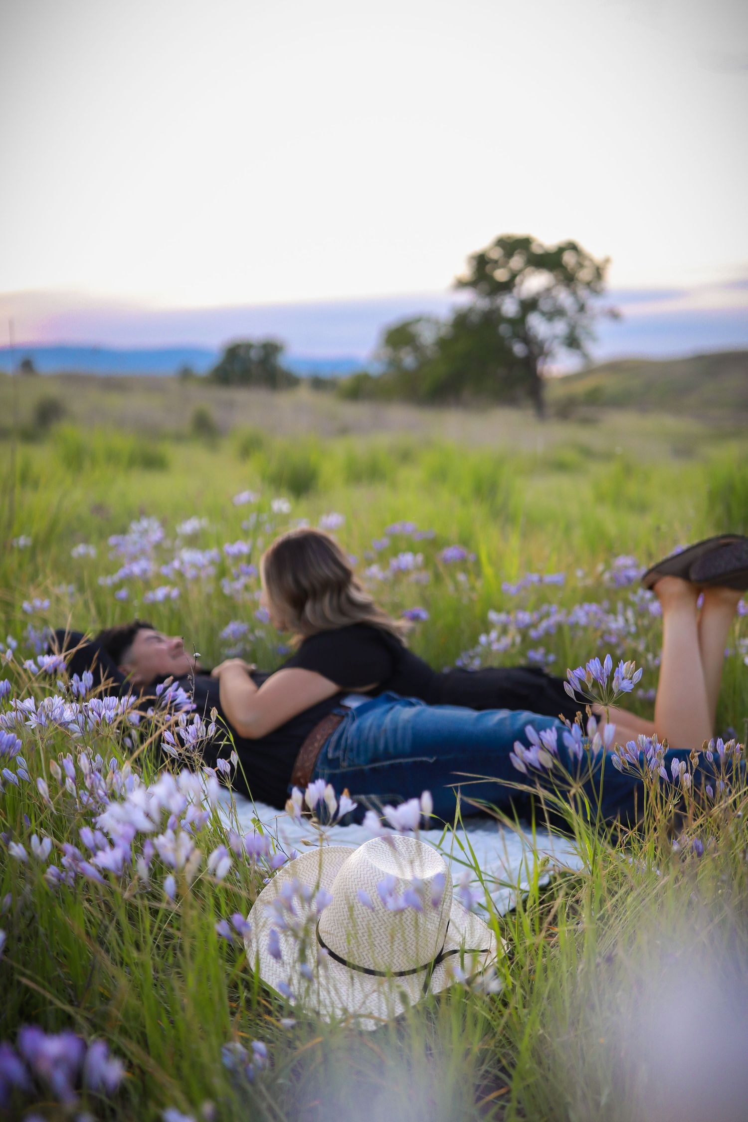Couple relaxing in a meadow of purple wildflowers at sunset with mountains in the distance.