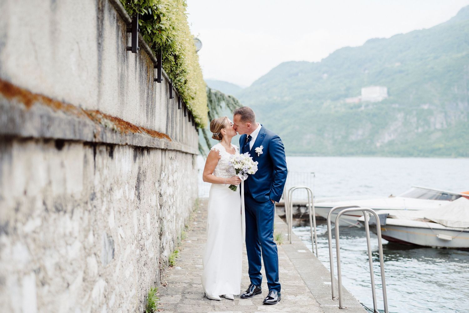 Coppia di sposi si scambia un bacio passeggiando su un molo in riva al Lago di Como