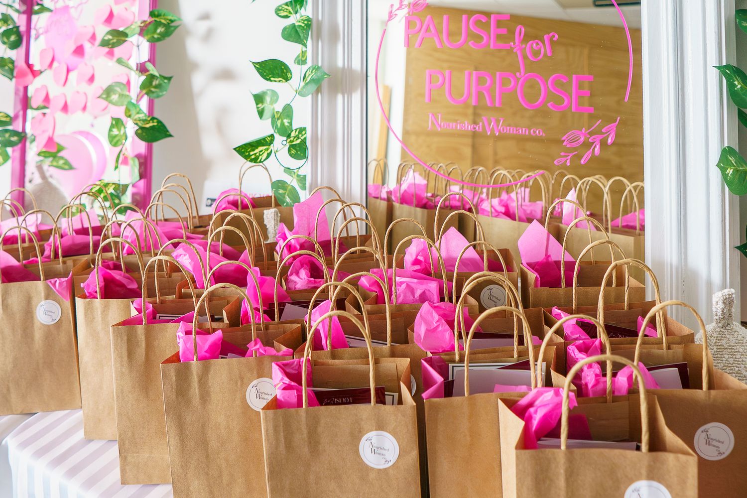 Brown kraft gift bags filled with hot pink tissue paper arranged for a Pause for Purpose women's event.