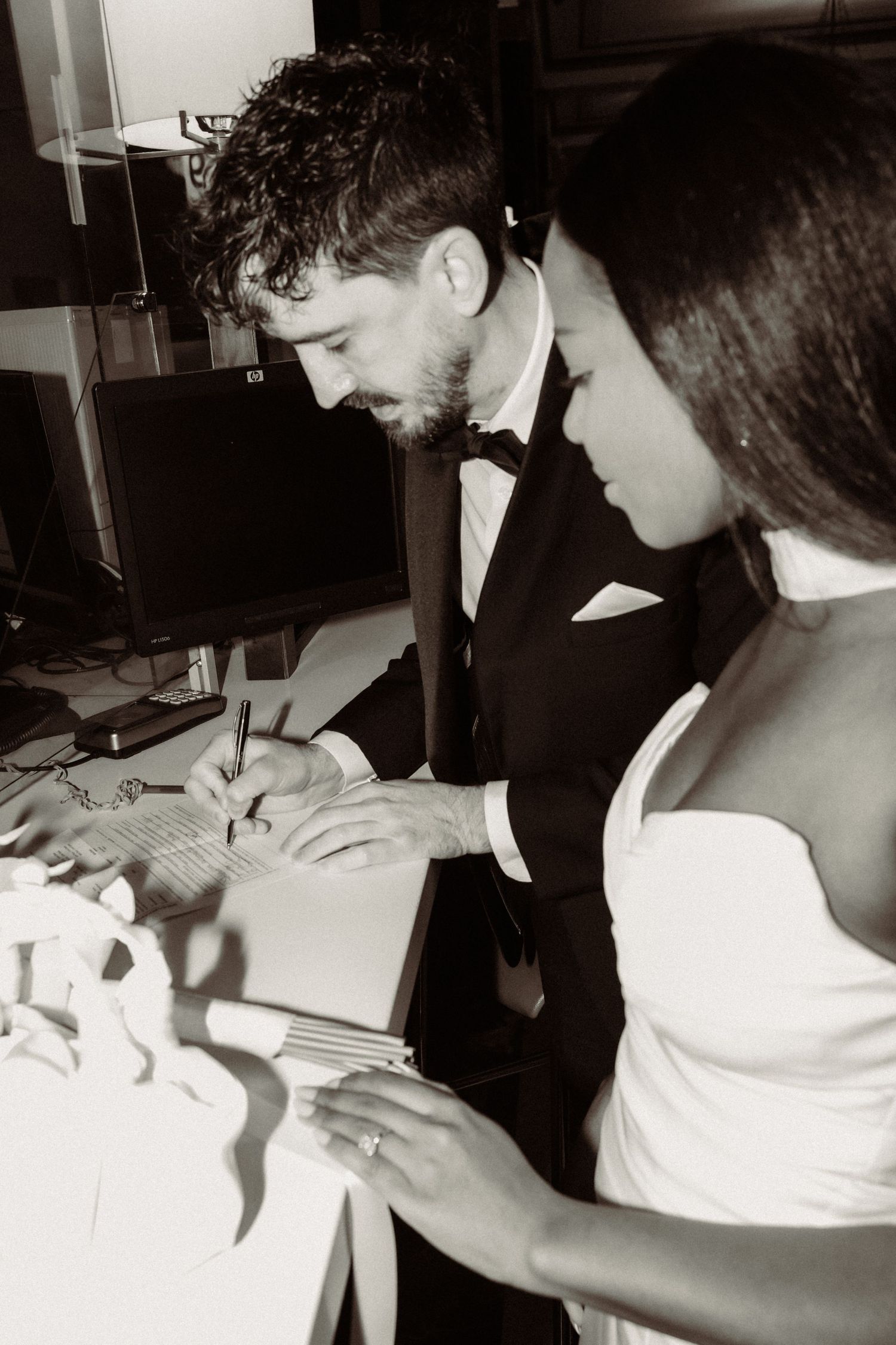 A classic black and white photo of a couple signing wedding documents at a table.