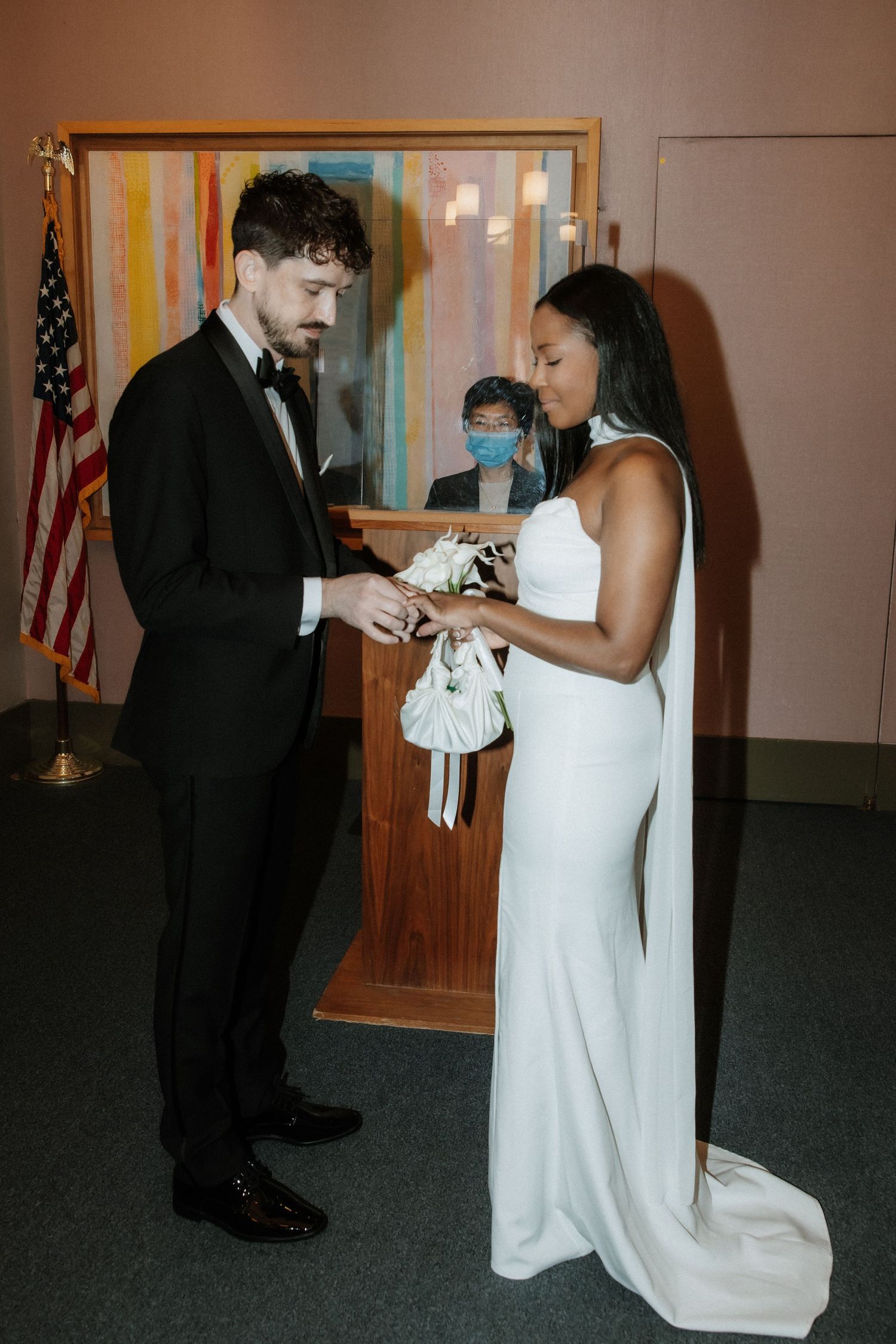 Couple exchanges rings during an indoor wedding ceremony with an American flag in the background.